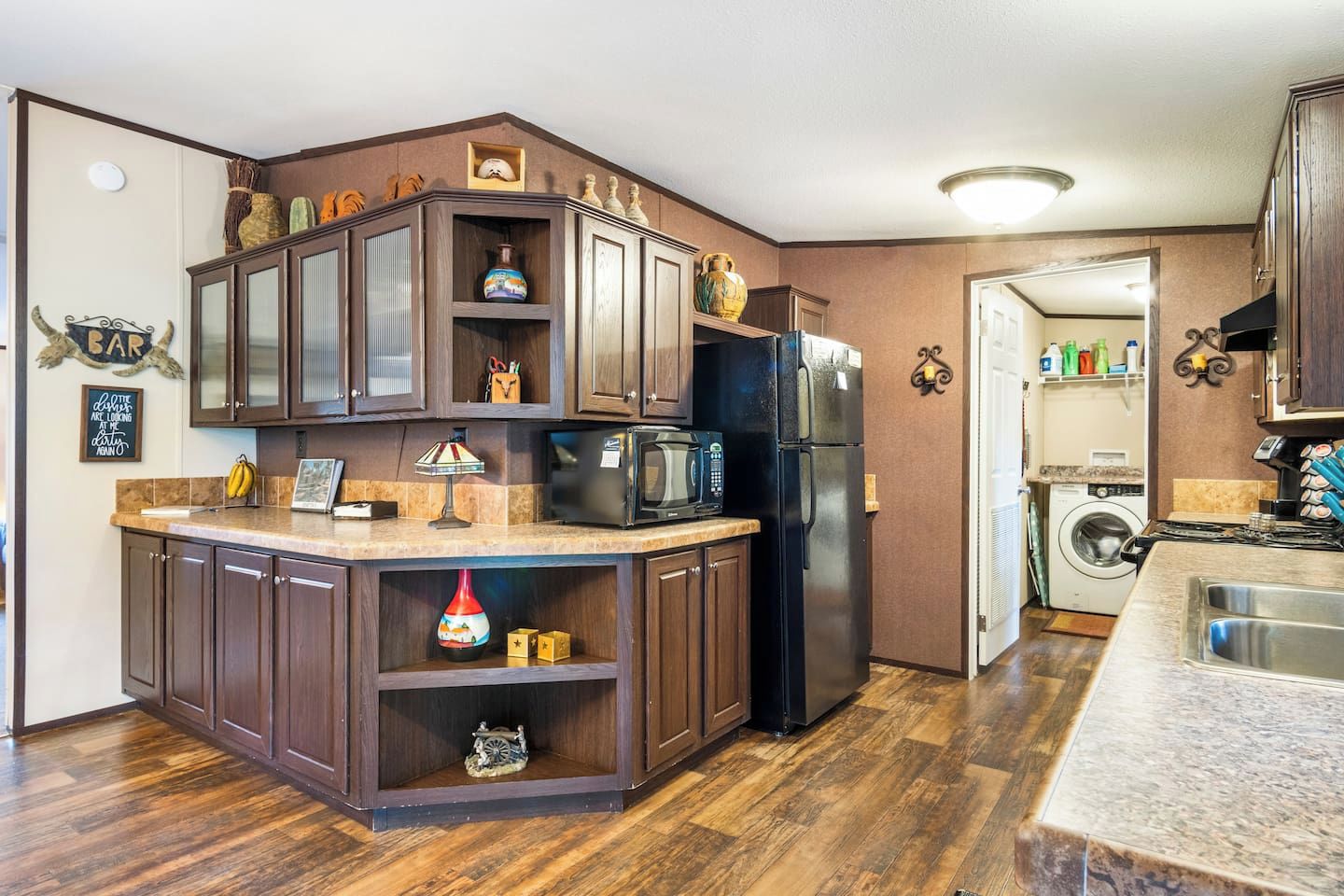 A compact kitchen with dark wood cabinets, a built-in microwave, and a refrigerator.