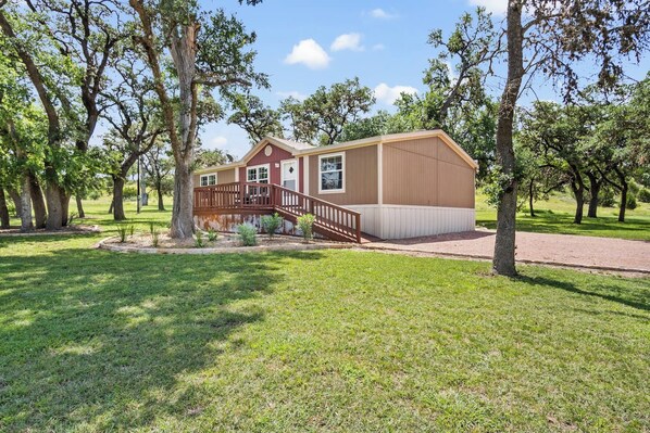 A single-story house with a front porch and a small deck, surrounded by trees and grass.