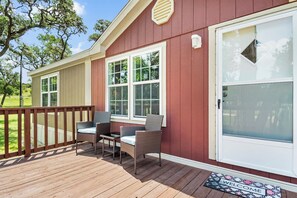 A wooden deck with outdoor furniture, a white door with a window, and a welcome mat.
