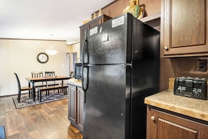 A kitchen with a black refrigerator, wooden cabinets, a dining table with chairs, a clock on the wall, and a toaster on the countertop.