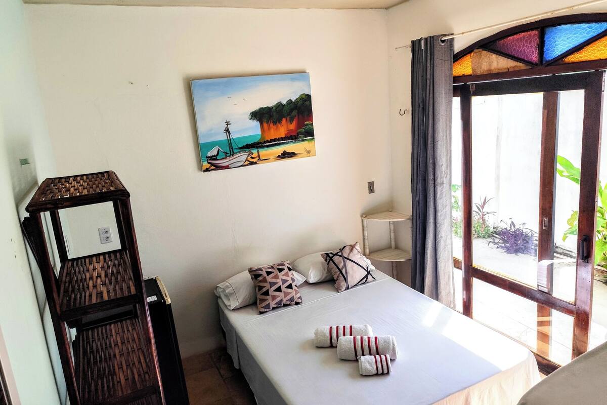 A bedroom with a bed, pillows, a painting, and a window with curtains.