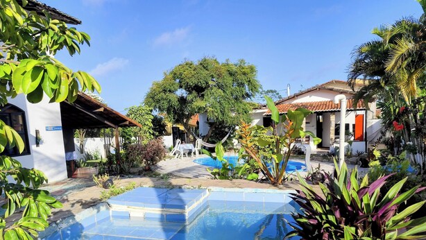 A pool area with a clear blue pool, surrounded by lush greenery and a white building with a tiled roof. -  Pipa Universo (Tibau do Sul)