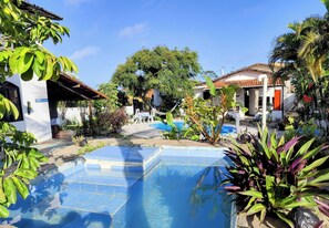 A pool area with a clear blue pool, surrounded by lush greenery and a white building with a tiled roof. - Pipa Universo (Tibau do Sul)