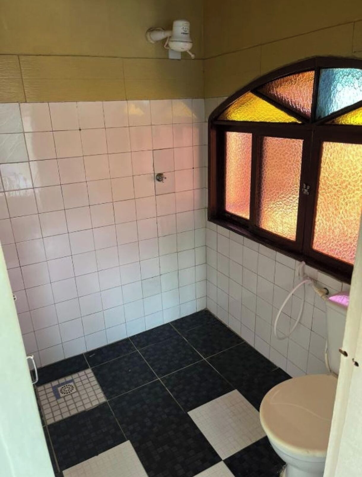 Ein kleines Badezimmer mit Toilette, Dusche und einem Fenster mit Buntglas.
