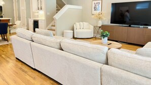 A modern living room with a large sectional sofa, a flat-screen TV, and a staircase leading to another level. - Modern 3BR Townhome w/Garage - Walk to Midtown/Downtown Tallahassee & FSU (Tallahassee)