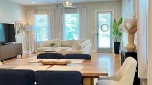 A modern living room with a sofa, dining table, chairs, and pendant lights. - Modern 3BR Townhome w/Garage - Walk to Midtown/Downtown Tallahassee & FSU (Tallahassee)