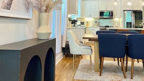 A modern kitchen with white cabinets, a dining area with blue chairs, and a wooden floor. - Modern 3BR Townhome w/Garage - Walk to Midtown/Downtown Tallahassee & FSU (Tallahassee)