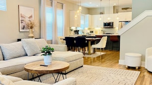 A modern living room with a sofa, coffee table, and a dining area with chairs. - Modern 3BR Townhome w/Garage - Walk to Midtown/Downtown Tallahassee & FSU (Tallahassee)