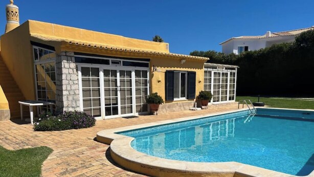 Un espace piscine avec une terrasse en pierre, un mur en pierre et un bâtiment jaune doté de grandes fenêtres.