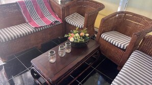 Un canapé en osier avec des coussins à rayures, une table basse en bois ornée d’un vase de fleurs et, au fond, un mur en pierre.