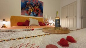 A hotel room with a bed, a painting on the wall, a bottle of wine, two glasses, and a lamp. - Vivenda Romana By Staywise (Lagos)