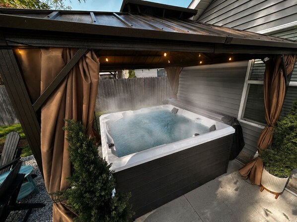 A hot tub under a covered patio with a wooden fence in the background.