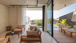 A modern living room with a sofa, coffee table, and chairs, a balcony with outdoor furniture, and a view of the surrounding area. - Designer Bungalow with Private Infinity Pool in Paphos (Chlorakas)