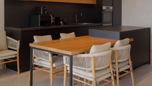 A modern kitchen with a central island, built-in appliances, and a dining area with a wooden table and wicker chairs. - Designer Bungalow with Private Infinity Pool in Paphos (Chlorakas)