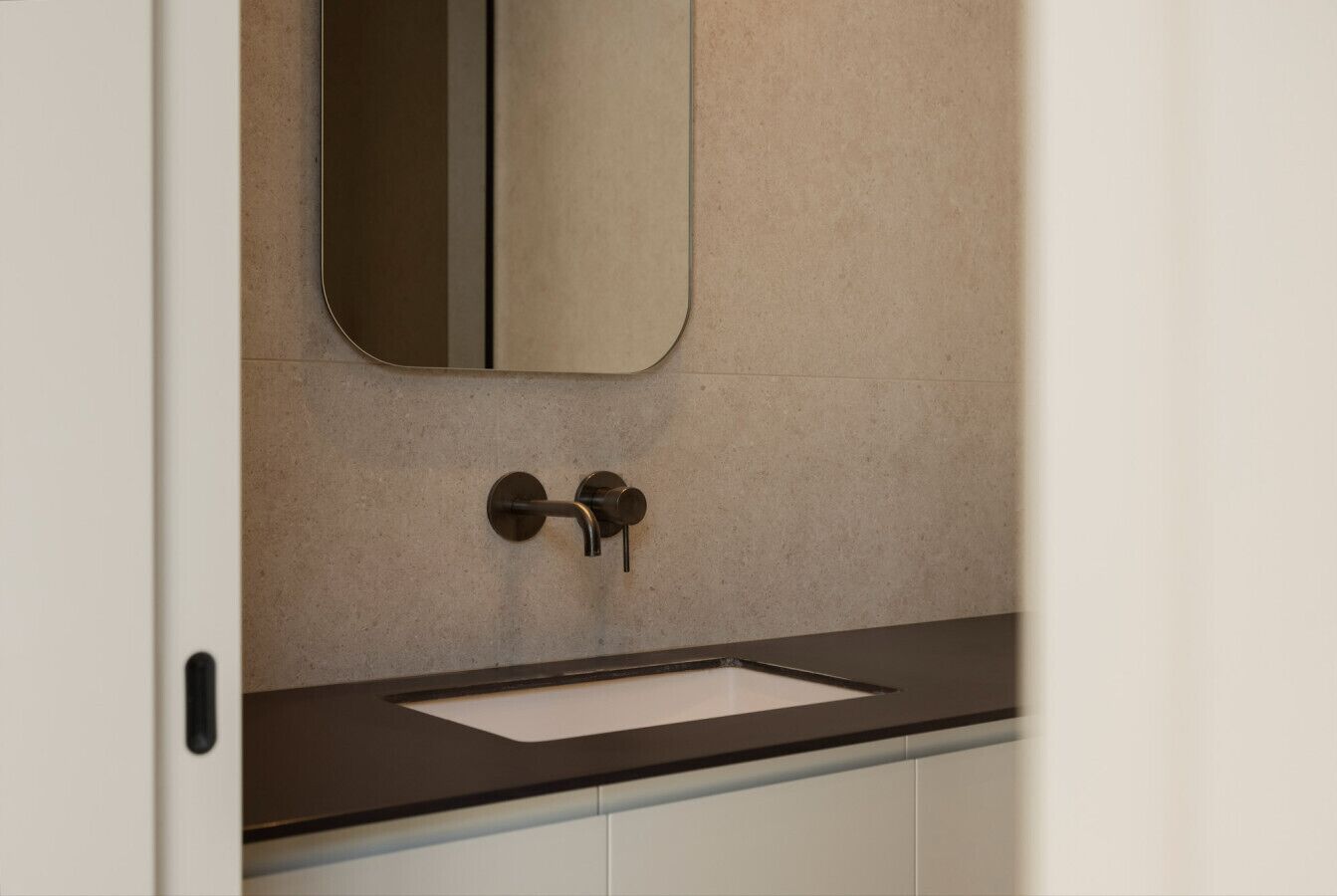 A bathroom with a white sink, a dark countertop, and a mirror above the sink.