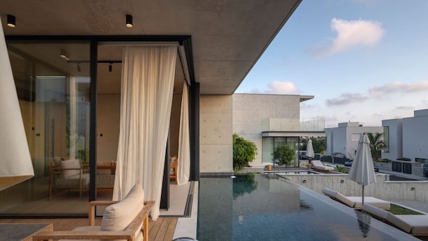 A modern outdoor pool area with a glass enclosure, lounge chairs, and a view of the surrounding buildings. - Designer Bungalow with Private Infinity Pool in Paphos (Chlorakas)