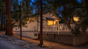 A cabin with a deck, surrounded by trees, and a gravel path leading to it. - Cedar Pines (Big Bear City)