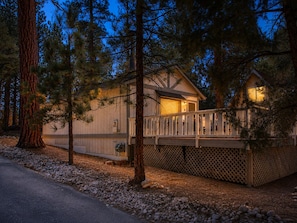 A cabin with a deck, surrounded by trees, and a gravel path leading to it. - Cedar Pines (Big Bear City)