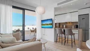 A modern apartment with a living room, dining area, and kitchen. It features a large window with a view of the sea, a flat-screen TV, and a dining table with chairs. - Estepona Beach Getaway! 2BR Apartment (Estepona)