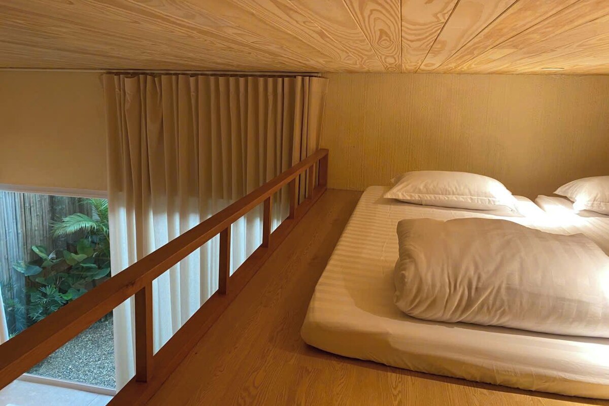 A bedroom with a wooden ceiling, a balcony with curtains, and a bed with pillows.