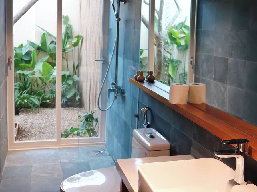 Ein modernes Badezimmer mit Toilette, Waschbecken und Dusche. Ein Fenster bietet Blick auf Grünflächen.