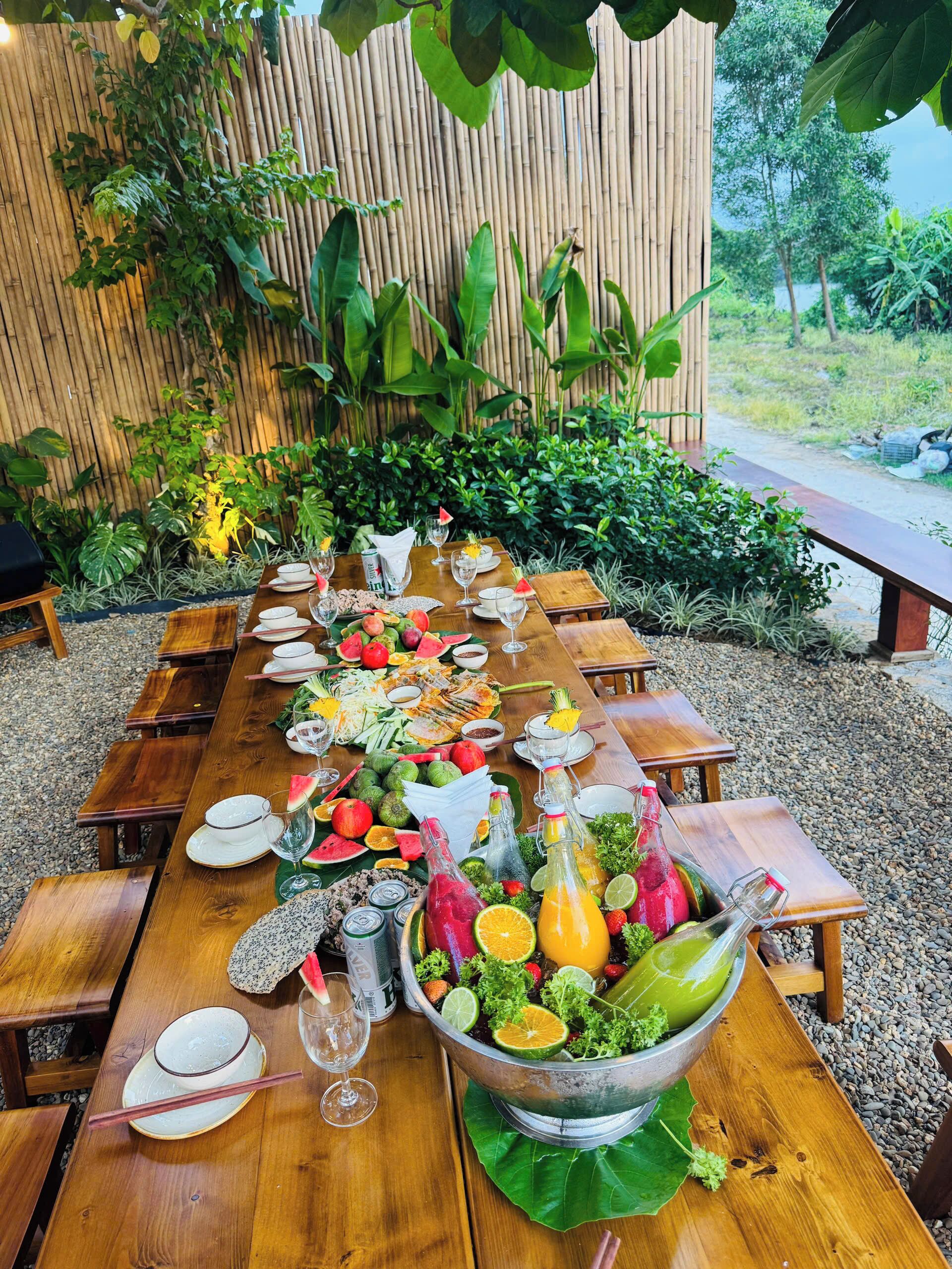 Een lange houten tafel gedekt voor een maaltijd, met diverse gerechten, drankjes en een grote saladeschaal.