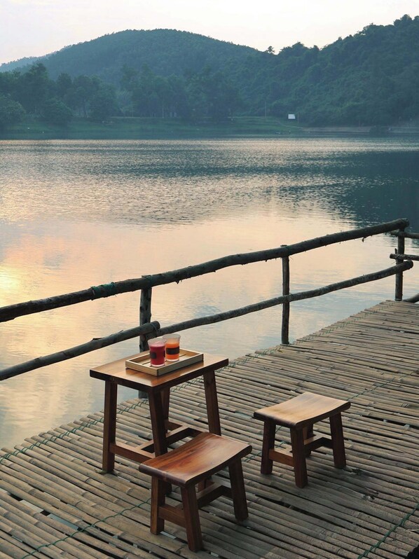 A wooden deck with a table and two benches overlooking a calm lake with a forested hill in the background. - Va Riverside Retreat (Hue)