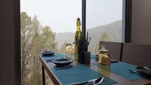 A dining table set with plates, cutlery, and a bottle, with a view of trees and hills through a window. - BluSalzz Escapade, Lansdowne - Uttarakhand (Lansdowne)
