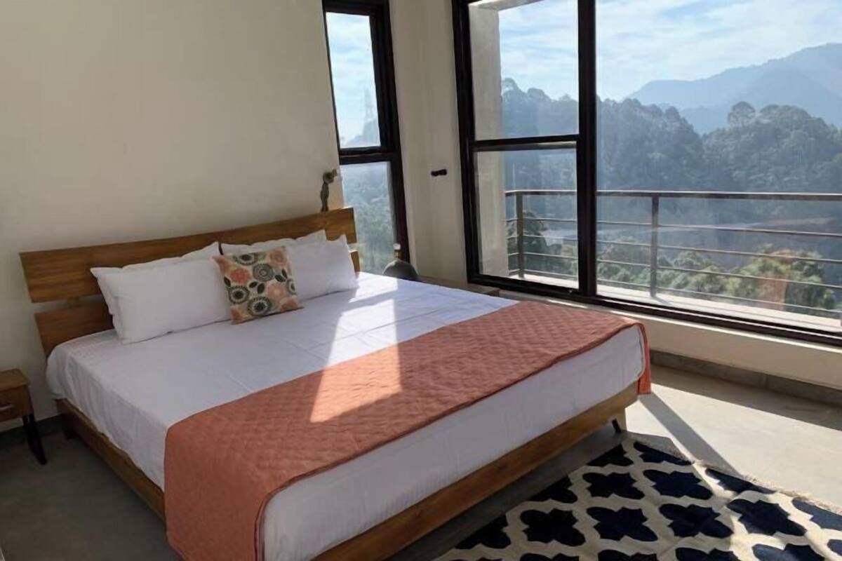 Camera da letto con un letto grande, una testata in legno e vista sulle montagne attraverso ampie finestre.