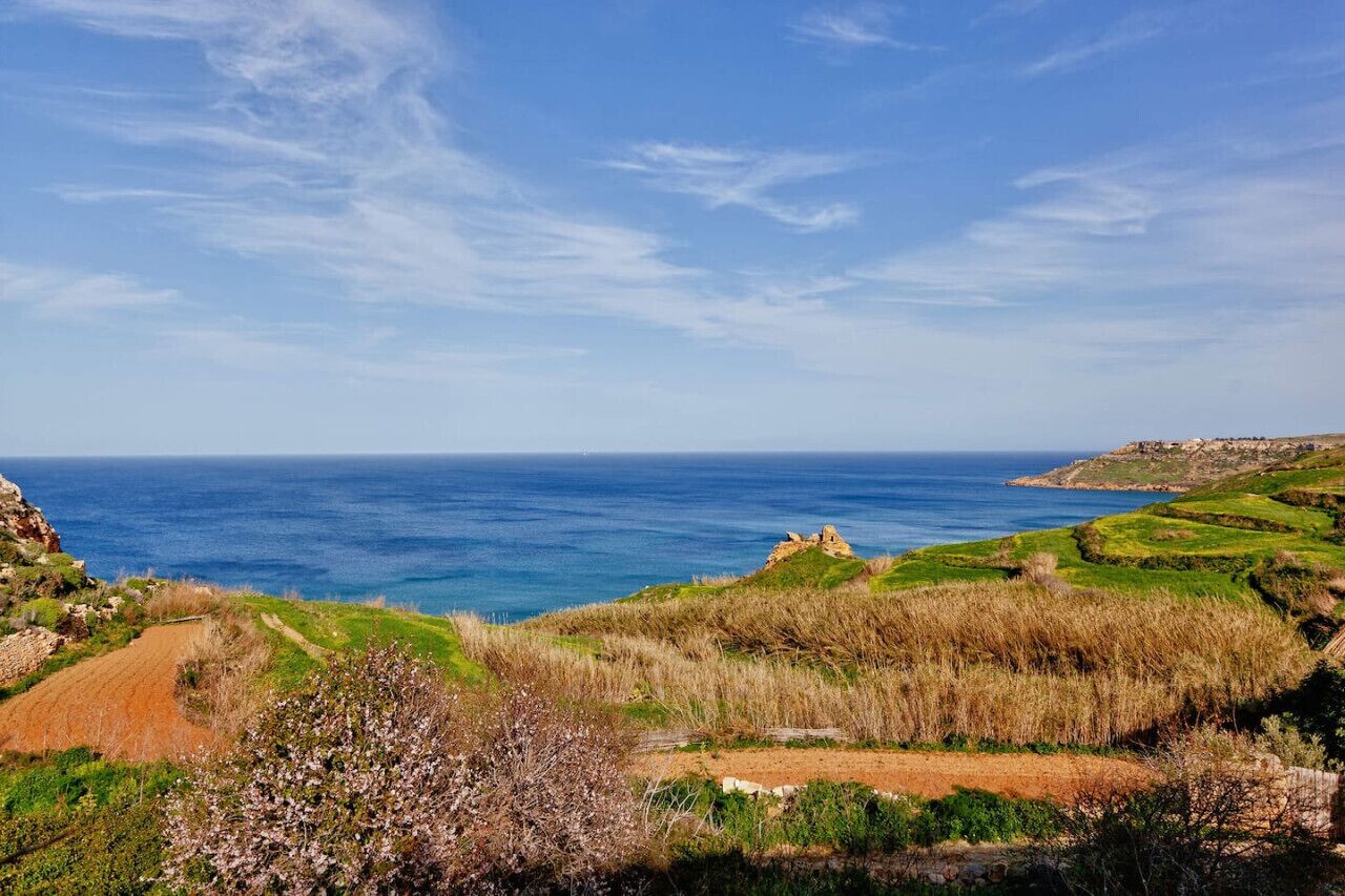 Un paisaje costero con vista despejada al mar, campos cubiertos de hierba y un afloramiento rocoso en la distancia.