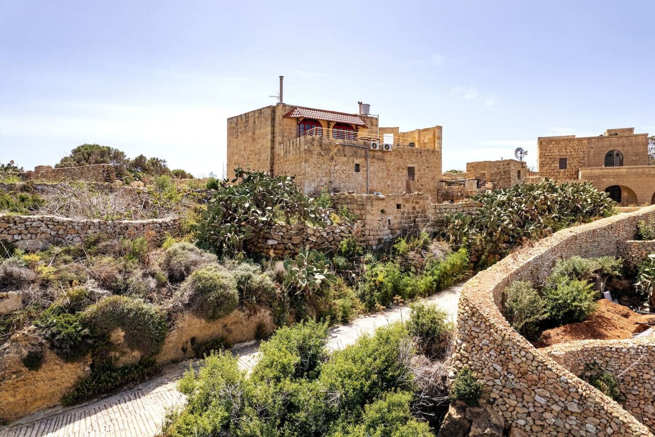 A stone-walled building with a flat roof and a windmill in the background.