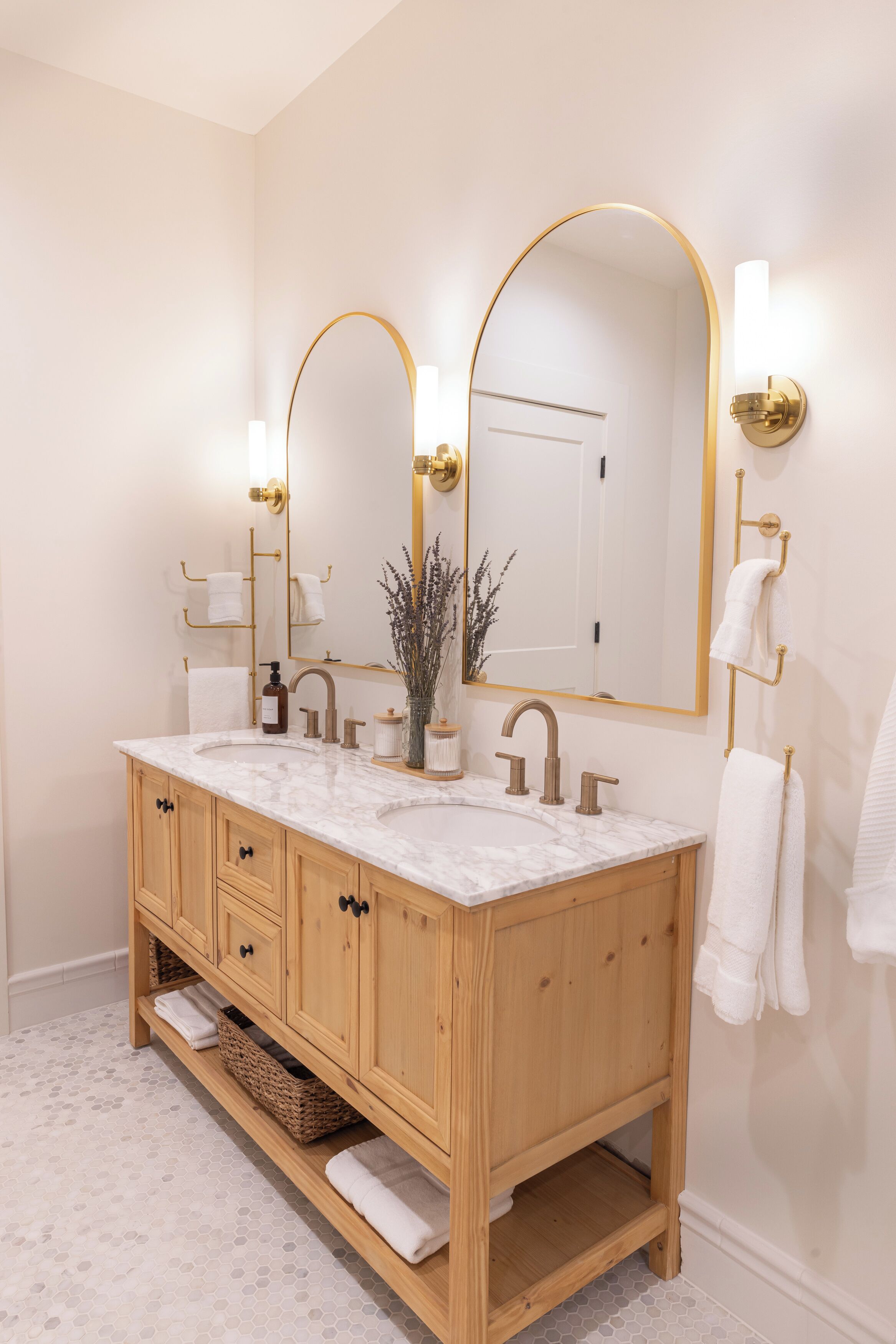 A bathroom with a wooden vanity, two sinks, a large mirror with gold accents, and a white door in the background.