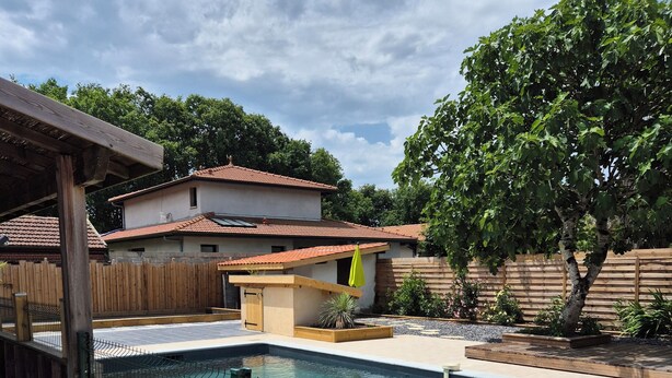 A swimming pool with a green fence, a wooden deck, and a house with a tiled roof in the background. - Family home in the heart of the Arcachon basin in Gujan Mestras (Gujan-Mestras)