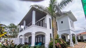 Une maison à deux étages avec un balcon, entourée d’une végétation luxuriante et dotée d’une allée pavée.