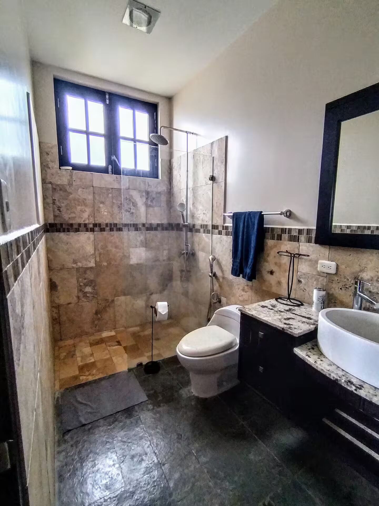 A bathroom with a shower, toilet, sink, and a window.