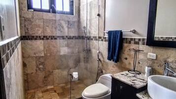 A bathroom with a shower, toilet, sink, and a window.