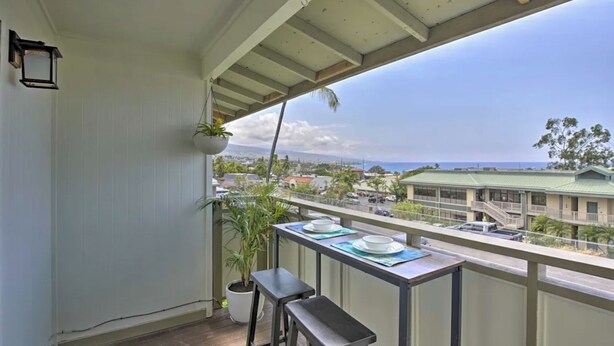 Un balcón con una mesa para dos, con vistas a un paisaje urbano con edificios y al océano.