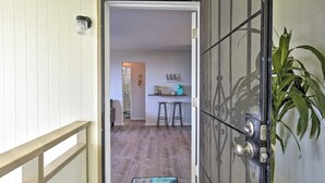 Una puerta que da a un cuarto con piso de madera, una pequeña zona de cocina con taburetes y una planta.