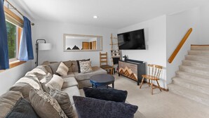 Een moderne woonkamer met een bank, een ronde salontafel, een aan de muur bevestigde televisie en een trap.