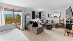 Een moderne hotelkamer met een groot bed, een bank, een tafeltje en een balkon met uitzicht op bergen.