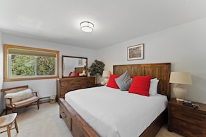 A bedroom with a large bed, wooden headboard, bedside tables, a bench, a window with a view of greenery, and a ceiling light. - Ww6709s3 (Silverthorne)