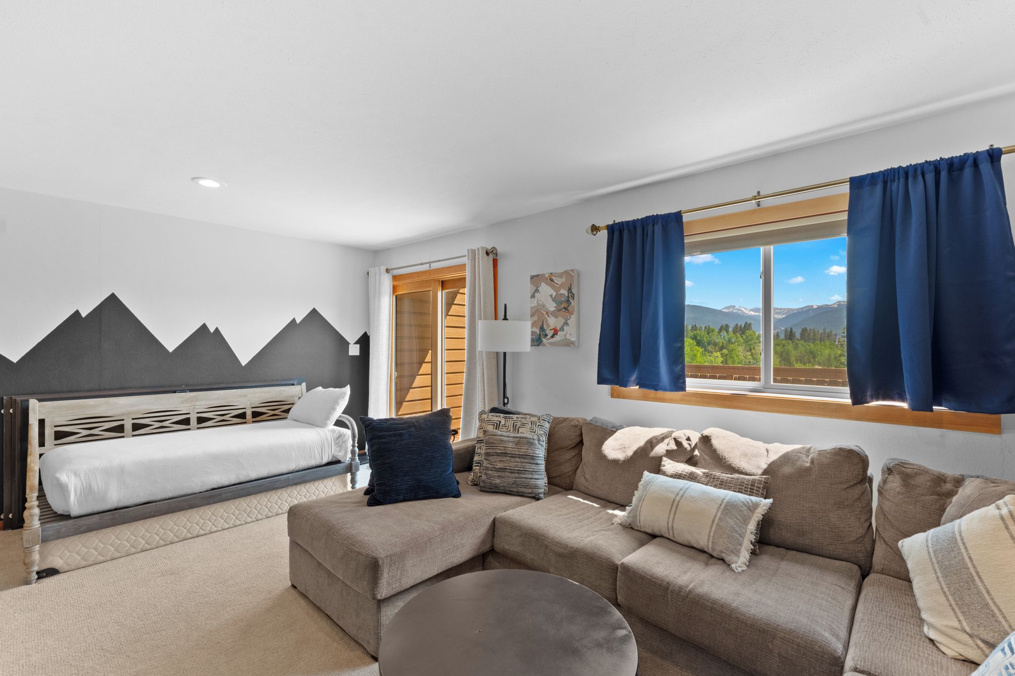 A modern room with a bed, sofa, and a view of mountains through a large window.