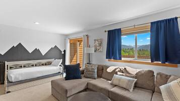 A modern room with a bed, sofa, and a view of mountains through a large window.
