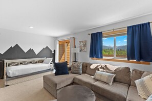 Une chambre moderne avec un lit, un canapé et une vue sur les montagnes, visible à travers une grande fenêtre.