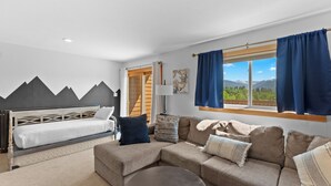 Een moderne kamer met een bed, een bank en uitzicht op bergen door een groot raam.