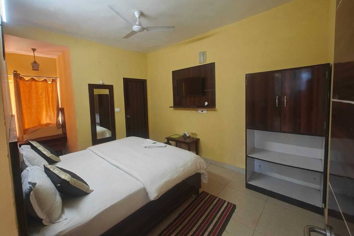 A bedroom with a bed, a ceiling fan, a TV mounted on the wall, and a wardrobe.