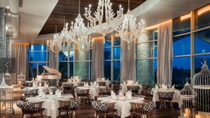 A dining area with multiple tables, chandeliers, and large windows.