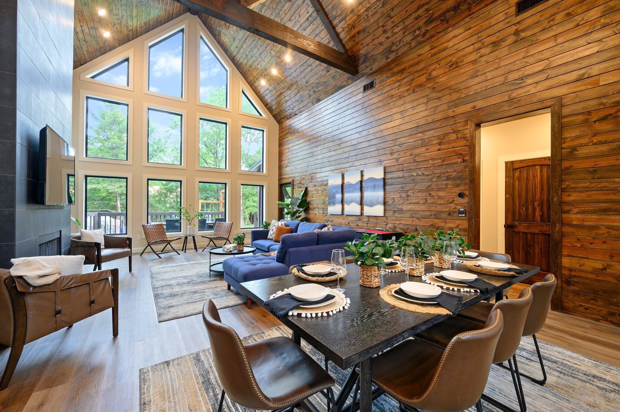 A spacious living area with a high ceiling, large windows, and a dining table set for six.