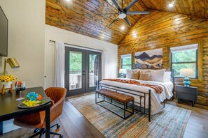 A bedroom with a bed, bench, desk, chair, and artwork. - Heated Pool•ColdPlunge•Sauna•HotTub•Firepit•Playground•Arcade•Heart of Hochatown (Broken Bow)