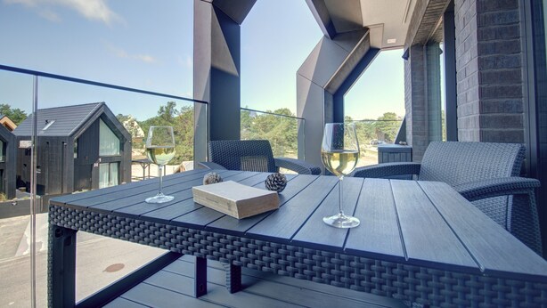 Un área de comedor al aire libre moderna con una mesa, sillas, un libro y una copa de vino.